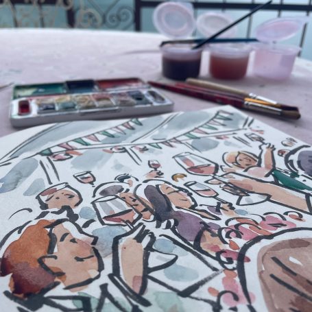 Foto einer Tuschezeichnung auf dem Tisch liegend mit Zeichenmaterialien, Große Menschengruppe erhebt ihre Gläser, koloriert